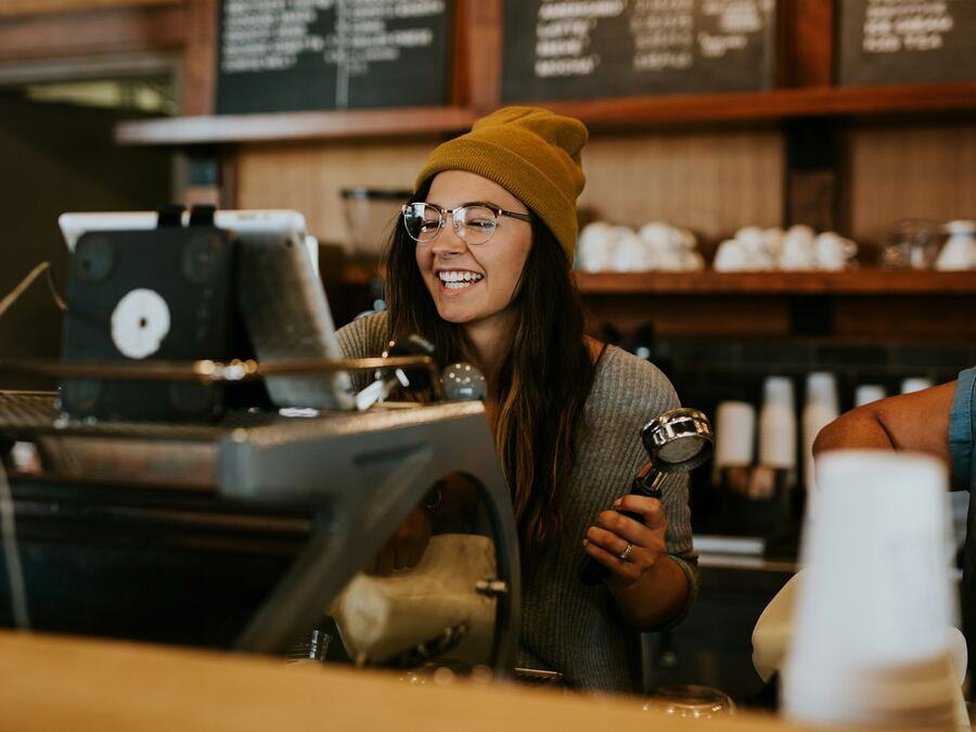 Barista souriante derrière le comptoir du café qu'elle vient d'ouvrir